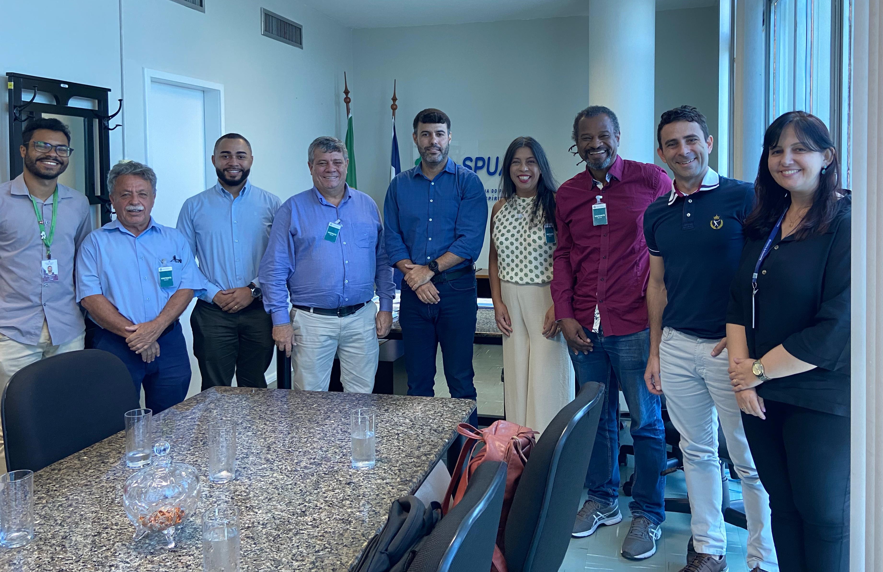 Foto da reunião na sala da SPU, com todos os presentes em pé, envolta da mesa.