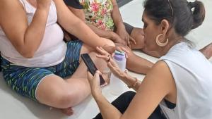 A imagem mostra três mulheres sentadas no chão, sendo que uma delas orienta as demais sobre o uso do aplicativo. 