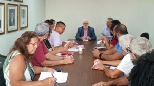 Pessoas presentes na reunião, sentadas em volta de uma mesa de madeira, com o reitor da Ufes sentado na cabeceira