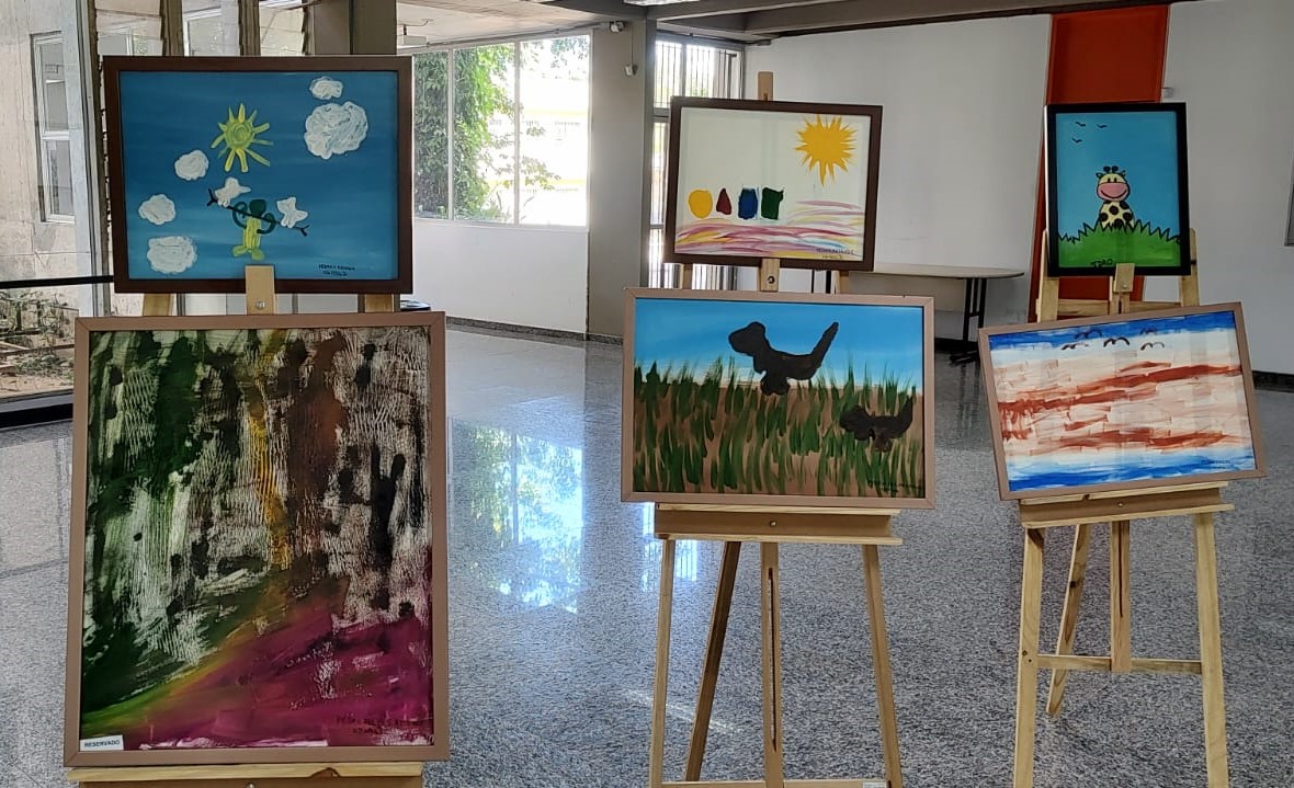 Foto com seis telas do artista, expostas em cavaletes no hall da Biblioteca Central da Ufes