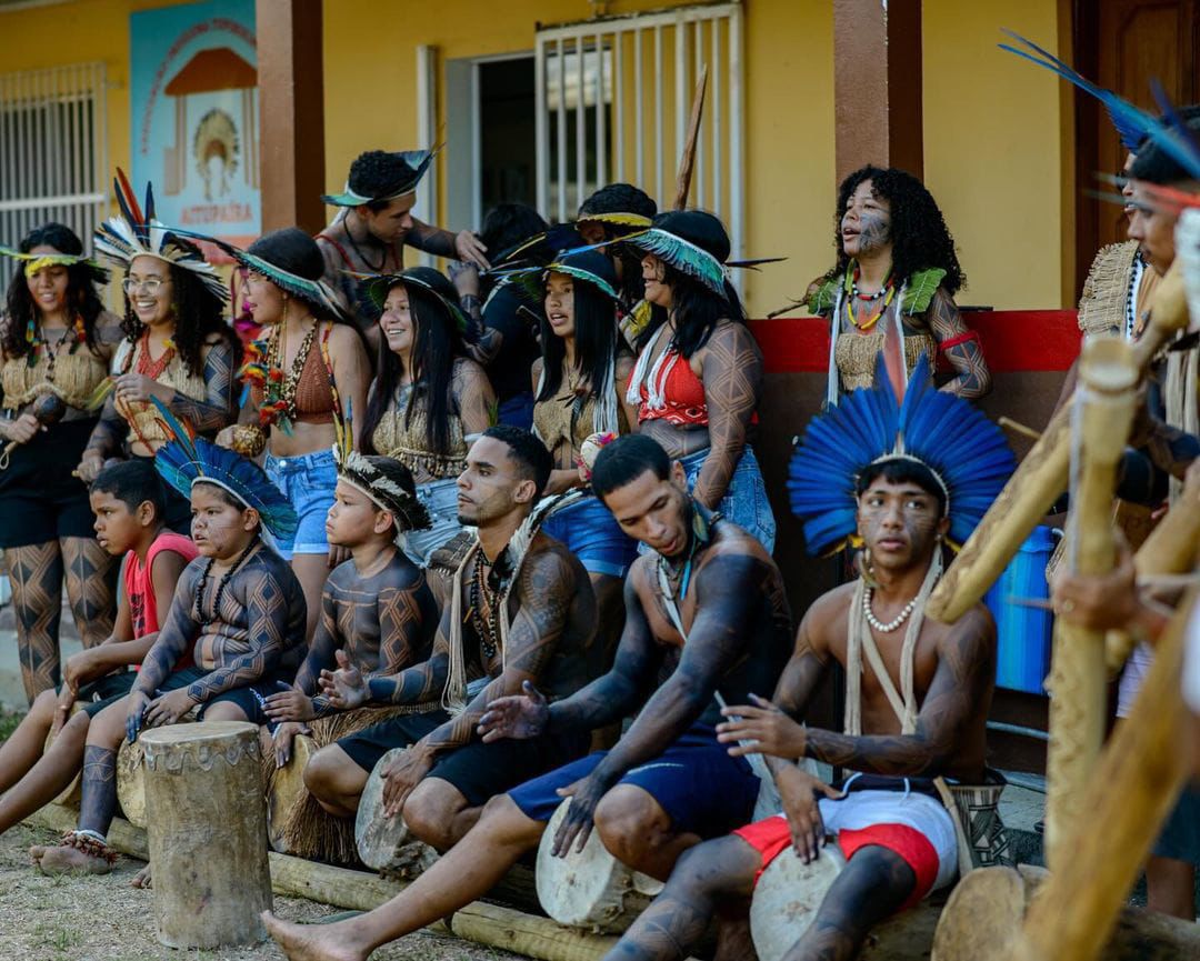 Grupo de dança Jovem Tupinikim, de Aracruz - ES Grupo de dança Jovem Tupinikim, de Aracruz - ES. A foto mostra um grupo de jovens indígenas com os corpos pintados usando cocares e acessórios indígenas. Alguns tocam pequenos tambores.