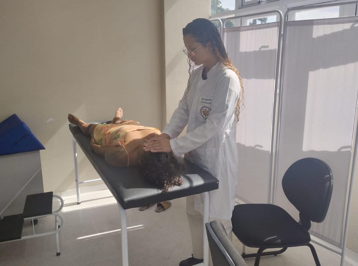 Profissional da Ufes aplica reiki em uma paciente deitada em uma maca.