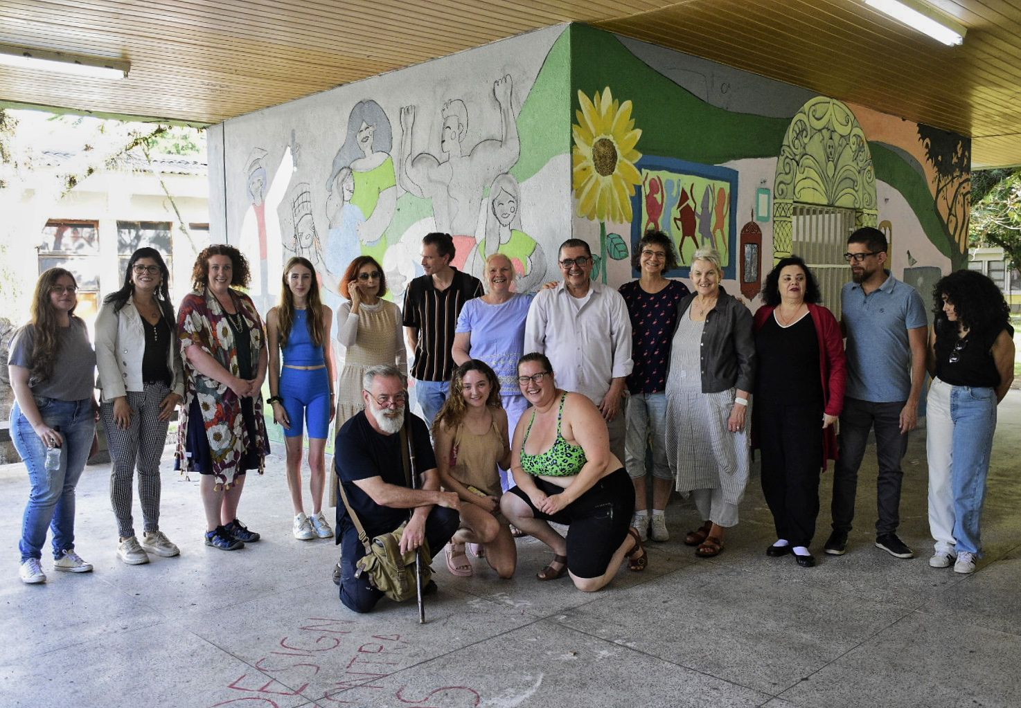 Grupo de professores e estudantes posam em frente ao painel que está sendo pintado