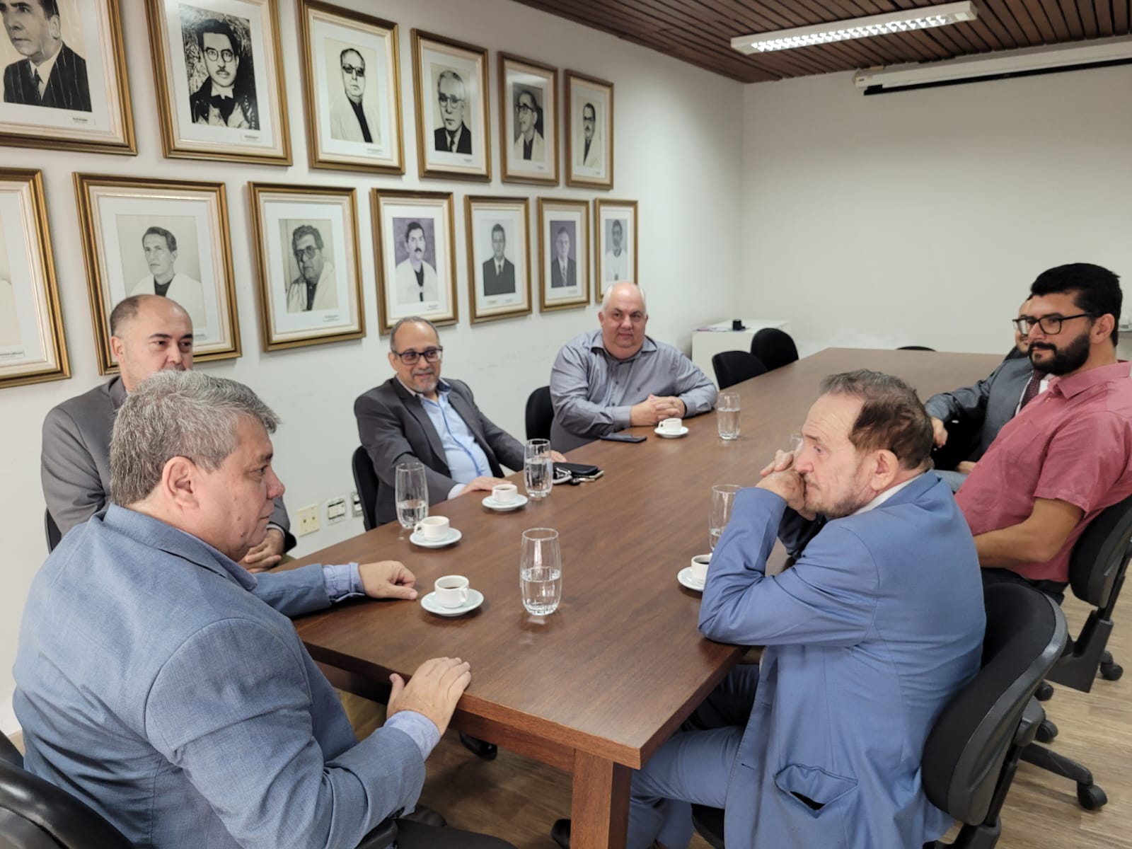 Foto dos participantes da reunião sentados em volta da mesa na sala de reuniões