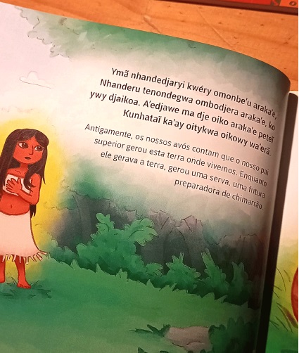 Foto da página de um livro infantil onde aparece um parágrafo escrito em língua indígena e, embaixo, em português