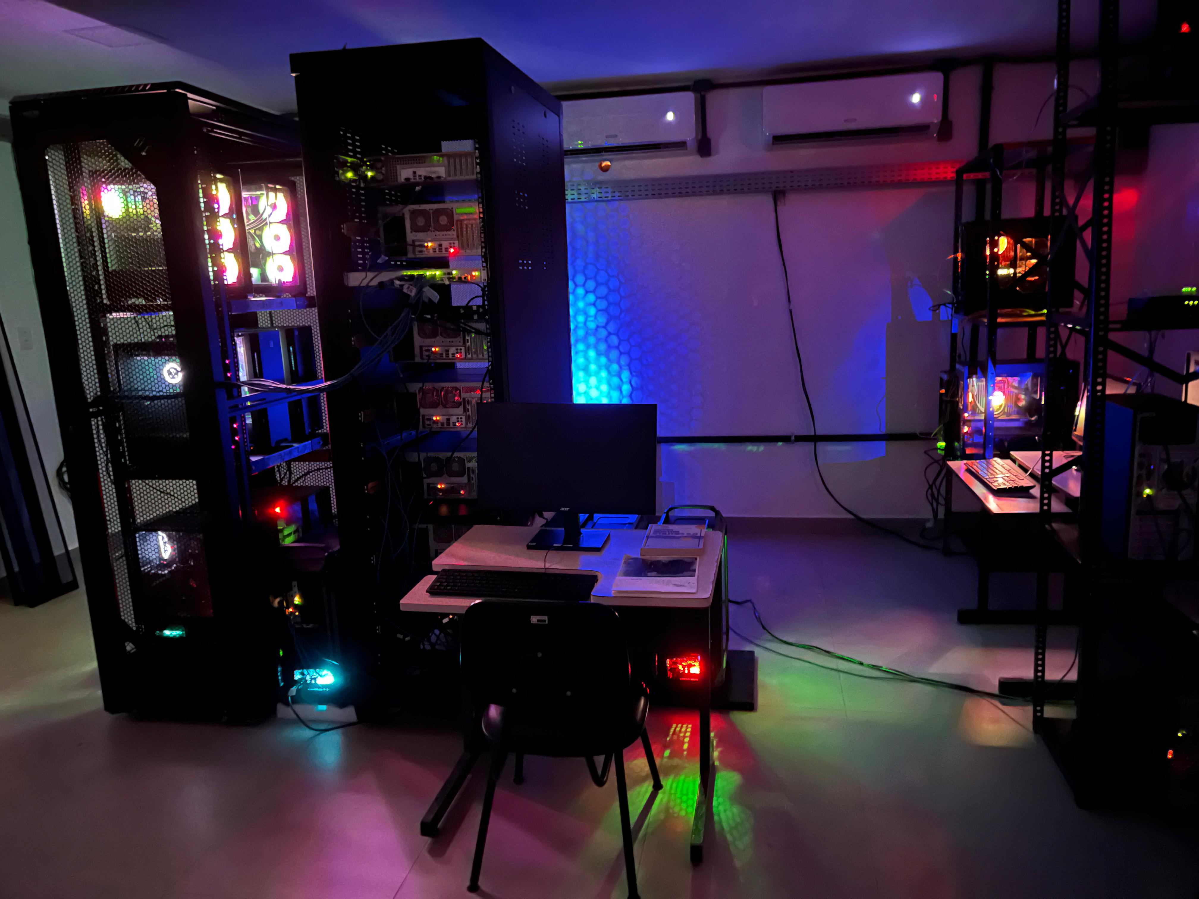 Foto do Laboratório Multiusuário de Computação Científica, onde aparecem estantes com computadores em um ambiente escuro com luzes coloridas