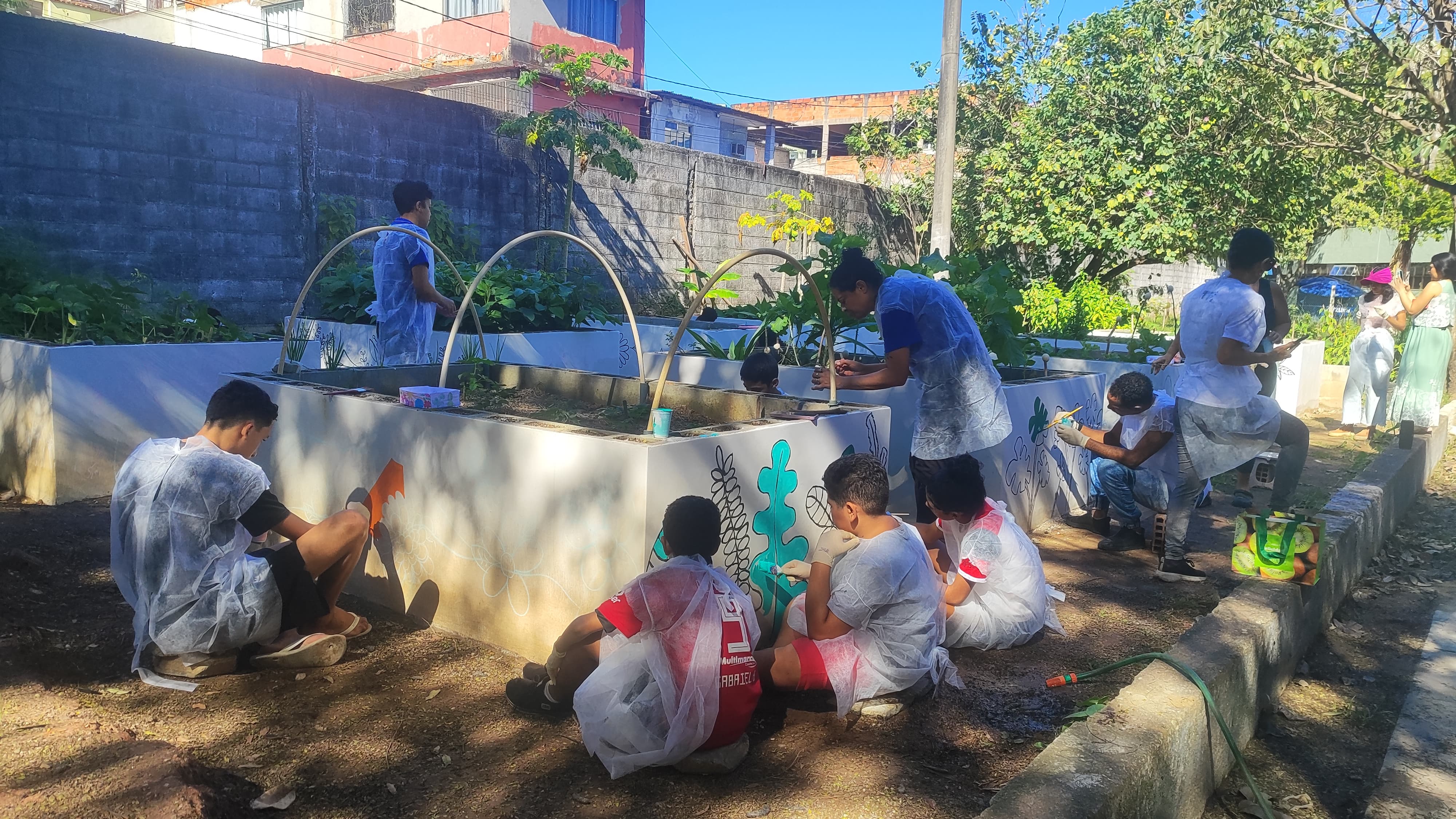 Foto de crianças e monitores pintando as paredes dos canteiros. 