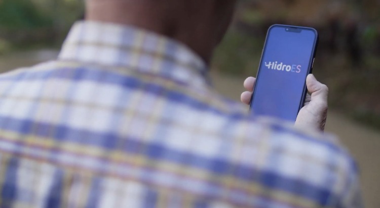 Foto de um homem de costas segurando um celular e, na tela, o nome HidroES