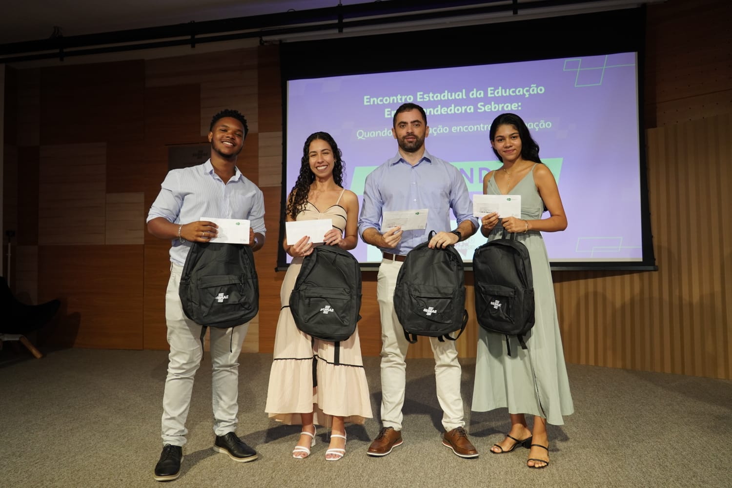 Foto dos estudantes premiados com o professor Gustavo Simão diante do painel de apresentação