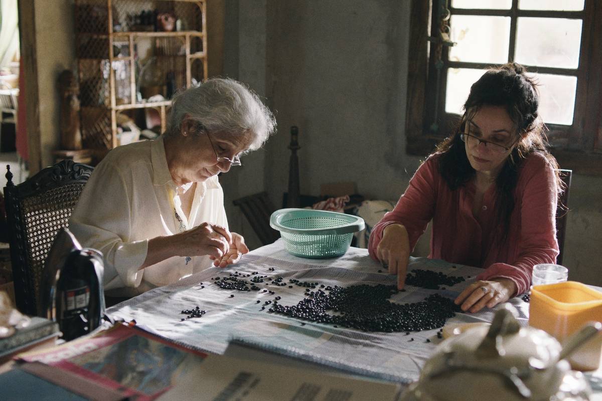 Cena do filme Malu, na qual duas personagens aparecem sentadas à mesa escolhendo feijão