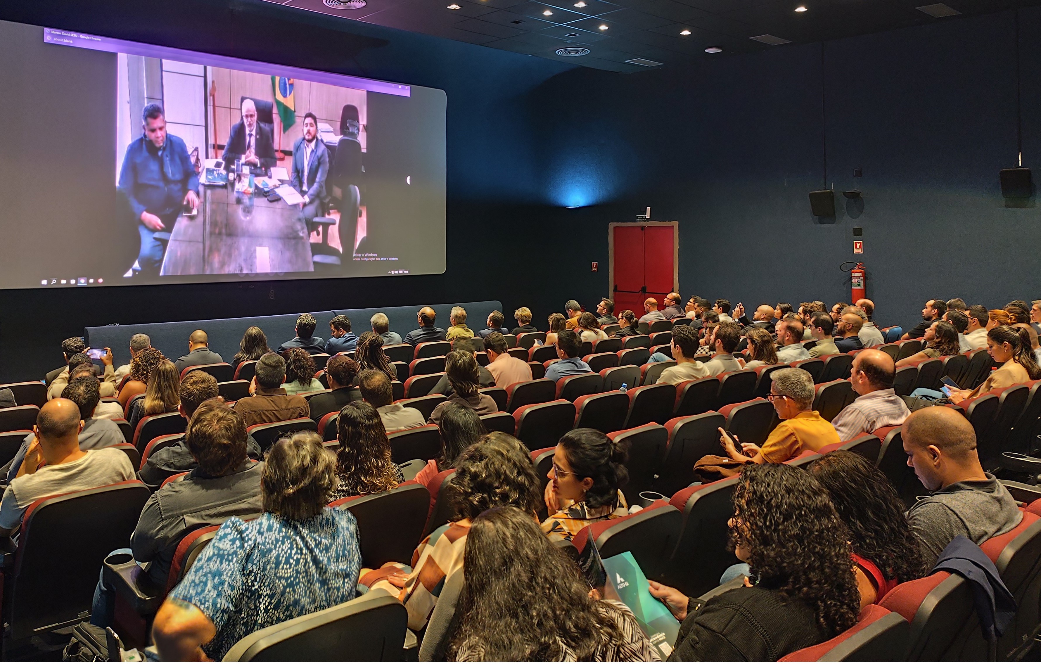 Foto dos participantes do evento no Cine Metrópolis. Na tela, a imagem do secretário de Educação Superior, que participou de forma remota.