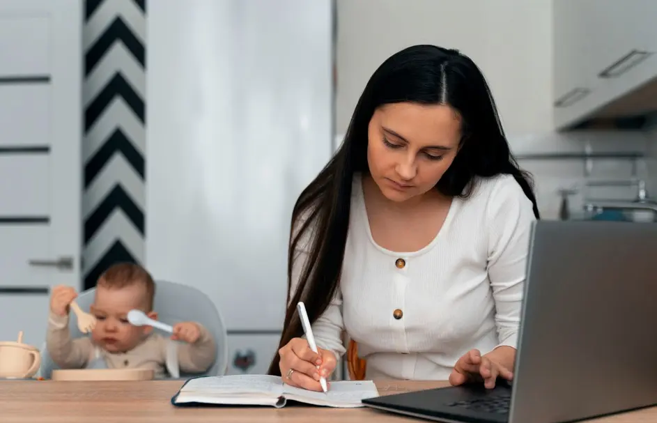 Imagem de uma mãe estudando, tendo ao lado um notebook e um bebê sentado em uma cadeirinha