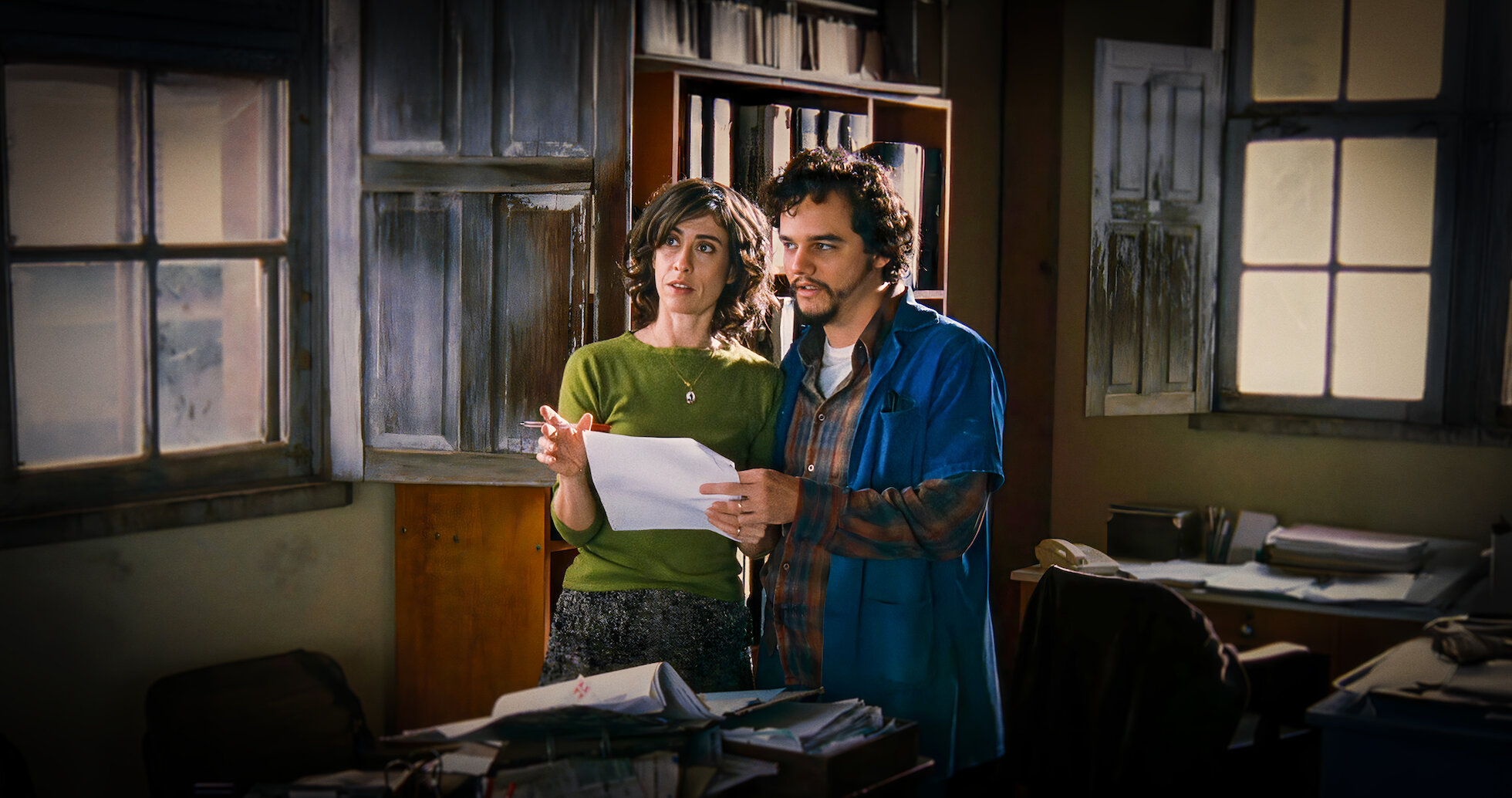 Cena de Saneamento Básico, o Filme Cena do filme Saneamento Básico, na qual dois personagens (uma mulher e um homem) estão em um escritório, segurando um papel nas mãos