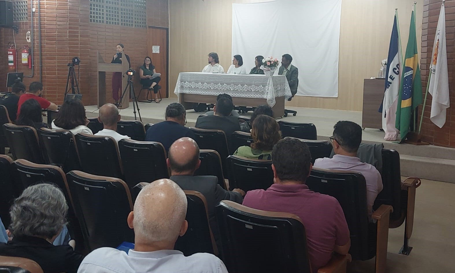 Foto da mesa principal da solenidade e de parte dos presentes no auditório