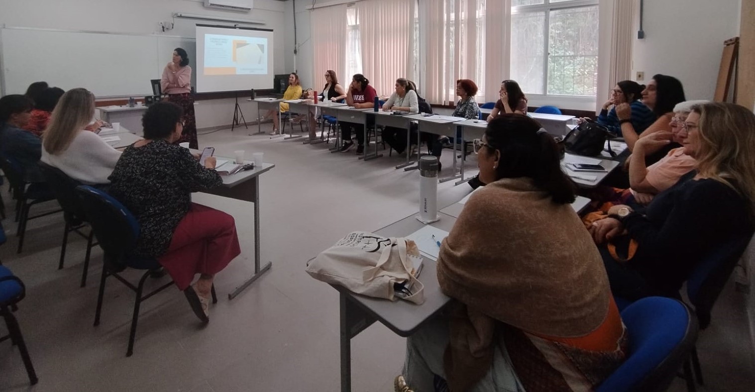 Foto de pessoas sentadas em círculo numa sala, ouvindo uma palestra 