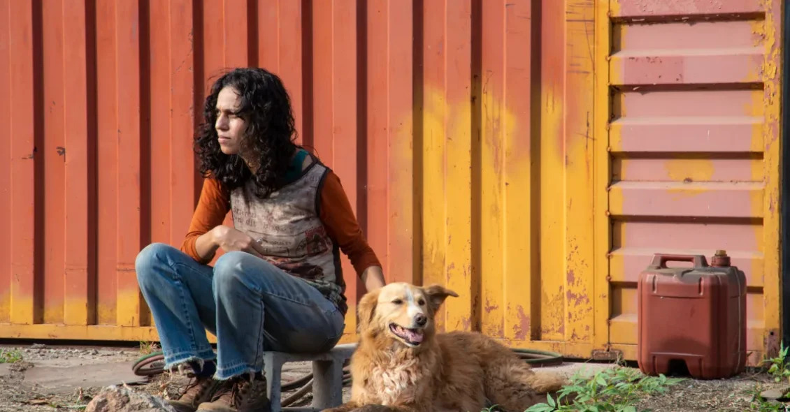 Cena do filme Suçuarana, onde aparece uma moça sentada em uma calçada, ao lado de um cachorro