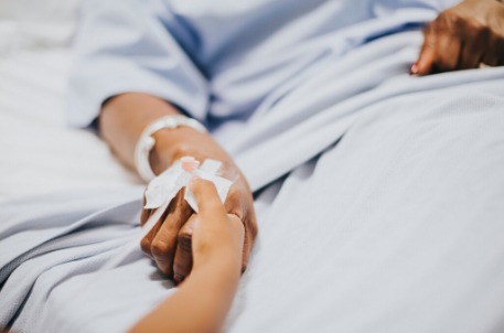 Imagem de uma mão segurando a mão de uma pessoa deitada em uma cama hospitalar