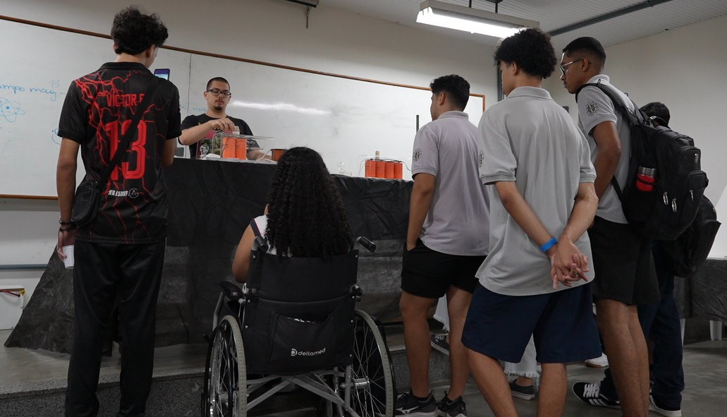 Foto de um grupo de estudantes vendo a apresentação de um experimento