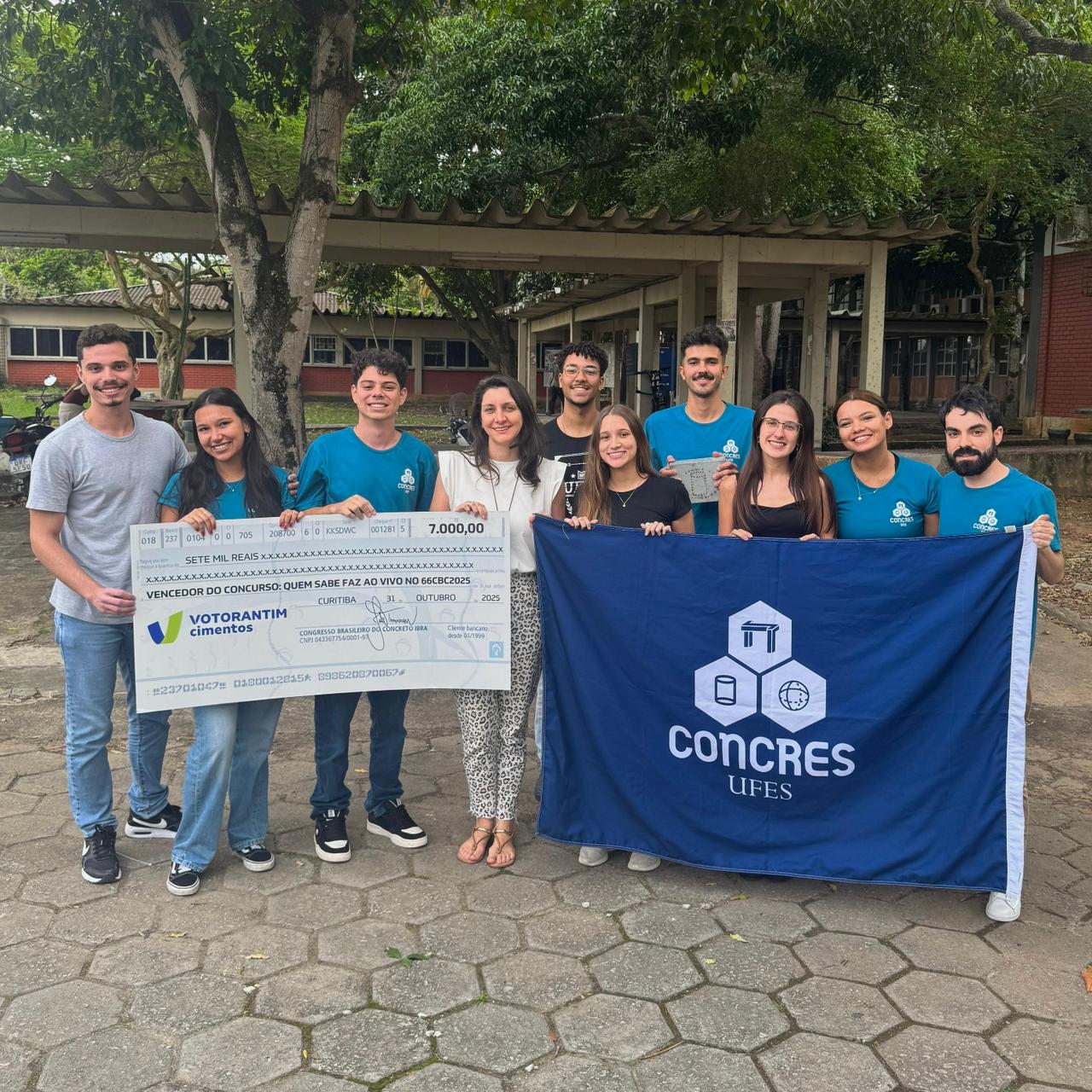 Foto dos estudantes segurando o cheque do prêmio e uma bandeira com o nome do projeto de extensão
