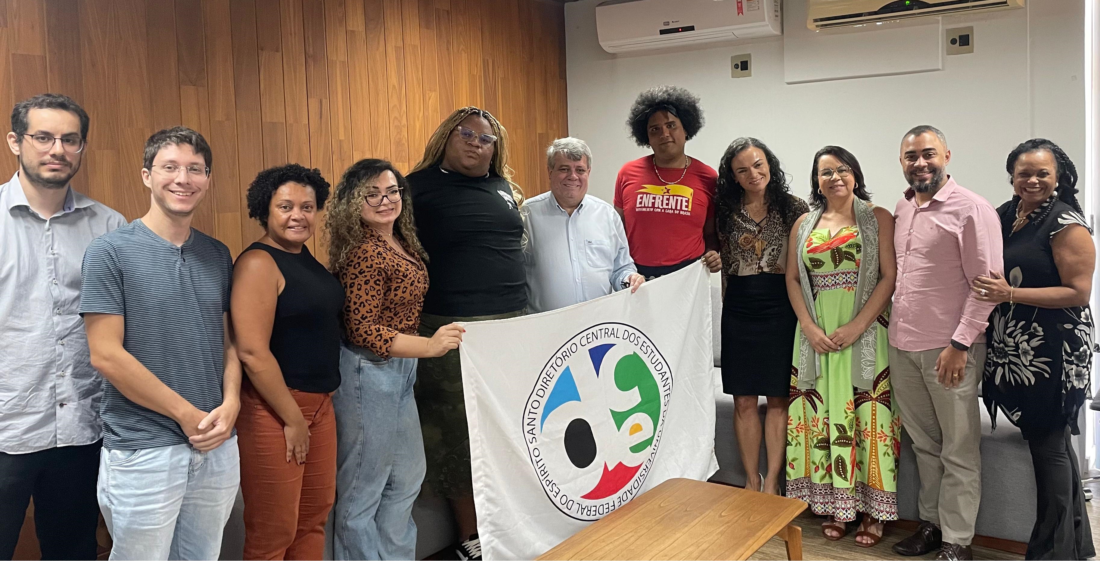 Foto dos participantes da reunião segurando a bandeira do DCE