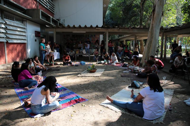 Foto da roda de conversa, com estudantes e lideranças indígenas sentados sobre cangas e esteiras, na área externa do Centro de Educação