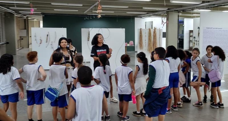 Foto dos alunos na exposição, ouvindo explicações da guia e da artista