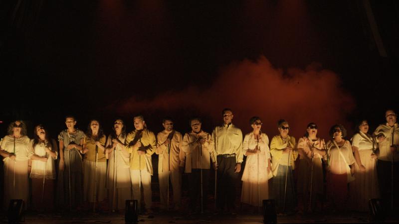 Cena da apresentação, com os cantores dispostos lado a lado no palco