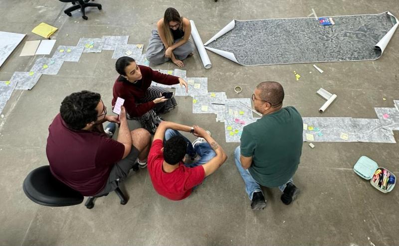 Foto de cinco pessoas discutindo o projeto com folhas de papel colocadas sobre o chão