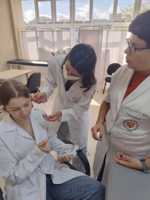 Foto de uma profissional aplicando estímulos na orelha de uma moça, com a ajuda de outra profissional