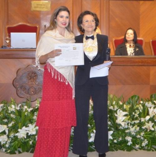 Foto da médica com um certificado em mãos na na Academia Nacional de Medicina,ao lado de uma senhora
