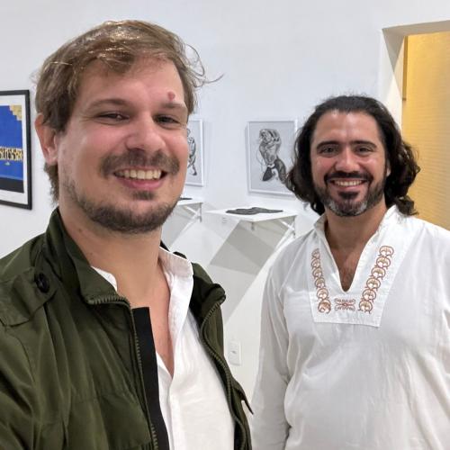 Foto dos estudantes João Cóser e André Magnago dentro da galeria, sorrindo para a câmera
