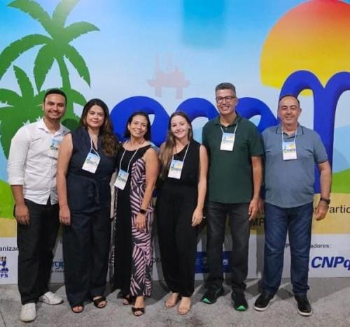 Foto dos professores e estudantes do Ceunes no congresso, com um painel com a logo do evento ao fundo