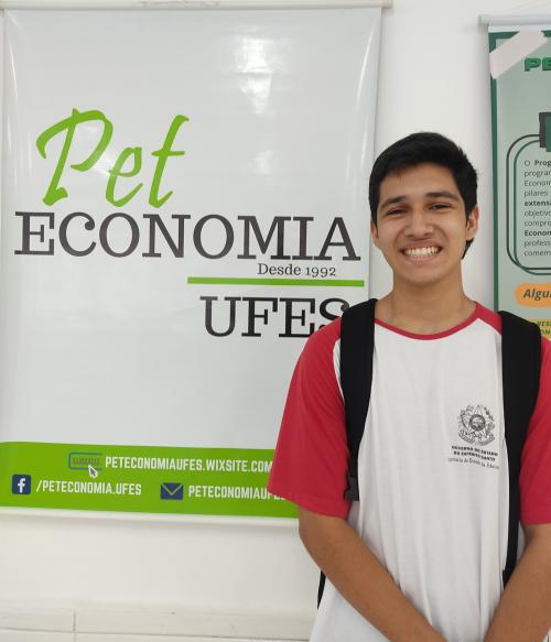 Foto do estudante João Gabriel sorrindo, ao lado de um banner do Pet Economia