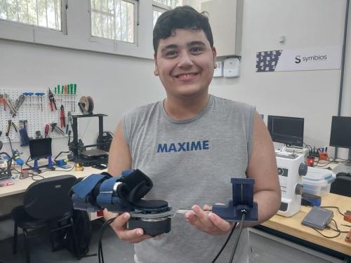 Foto do estudante Caio Zouain segurando a órtese robótica