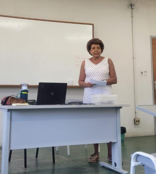 Foto da professora à frente de uma sala de aula