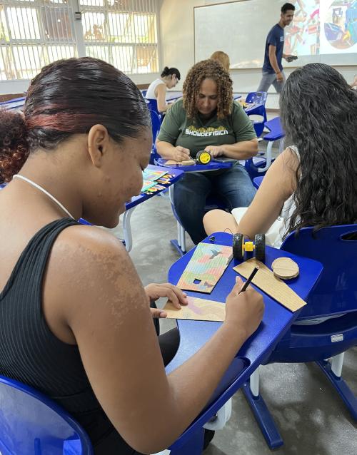 Foto de oficina na qual três participantes desenham sobre um pedaço de papelão