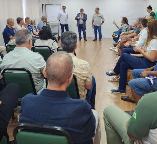 Vista geral da reunião, com as pessoas sentadas em cadeiras em uma sala. À frente, o reitor da Ufes com mais duas pessoas.