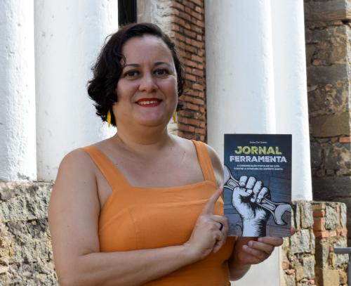 Foto da jornalista segurando um exemplar do livro