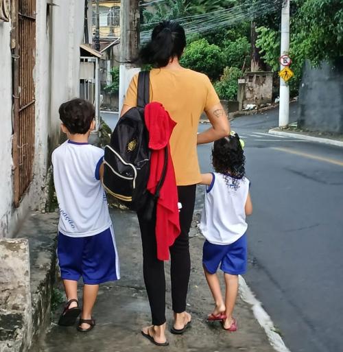 Foto de Ellen Bazoni de costas, andando em uma calçada e segurando dois filhos pela mão