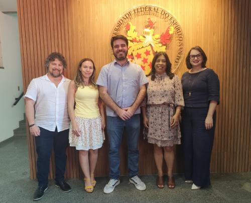 Foto dos professores e do vereador em pé, em frente ao brasão instalado no hall de entrada do prédio da Reitoria