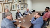 Foto dos participantes da reunião sentados em volta da mesa na sala de reuniões