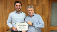 Foto do vereador Pedro Trés ao lado do reitor, ambos segurando o diploma da moção