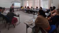 Foto de pessoas sentadas em círculo numa sala, ouvindo uma palestra 