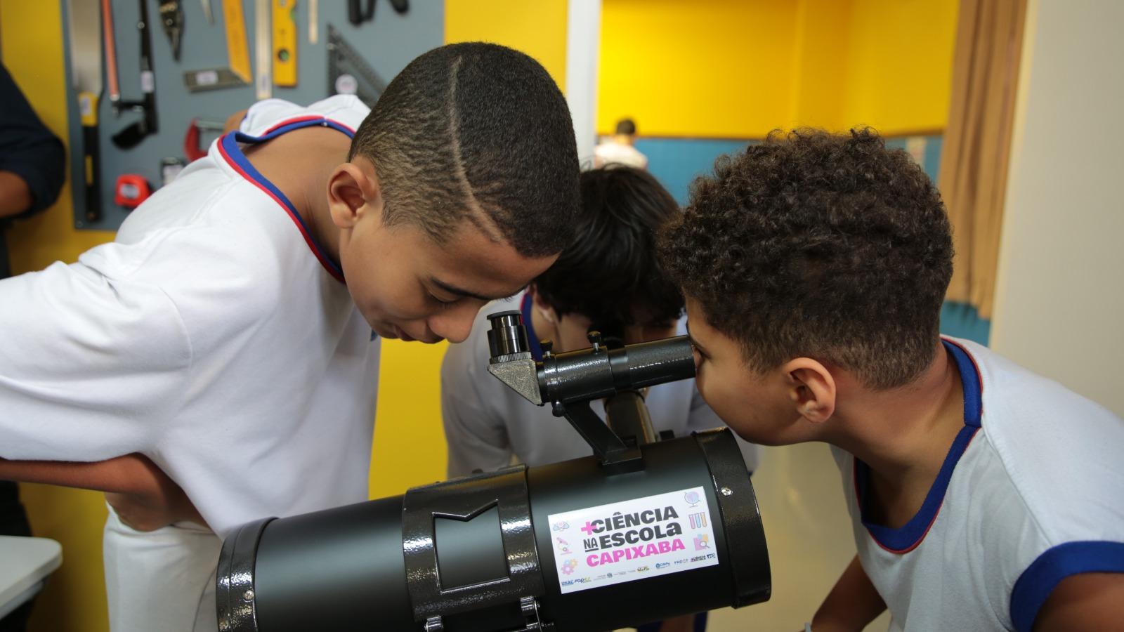 Foto de três alunos olhando para em um telescópio