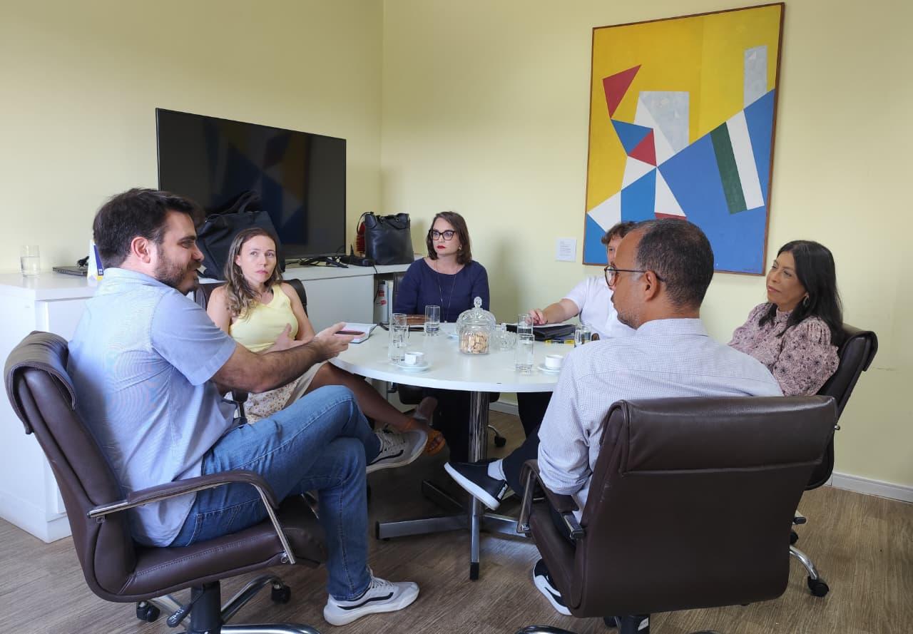 Foto dos participantes conversando sentados à mesa de reunião
