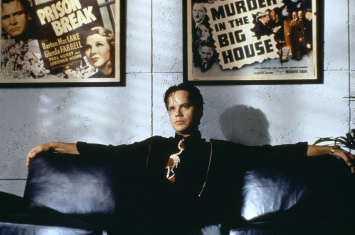 Cena de O Jogador, onde aparece o personagem principal sentado em um sofá com os braços abertos sobre o encosto