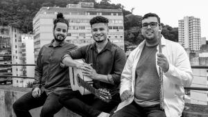 Foto em preto e branco de Léo de Paula, Luciano Furtado e Matheus Viana sentados na mureta de um viaduto, com prédios ao fundo.