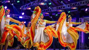 Grupo de dança Flor de Atalaia, do Mato Grosso do Sul Grupo de dança Flor de Atalaia, do Mato Grosso do Sul. A foto mostra quatro moças em um palco, dançando com vestidos brancos de saia rodada com detalhes em amarelo e vermelho.