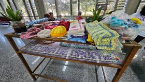 Mesa com as peças de crochê produzidas na oficina. Ao fundo, as participantes crochetando