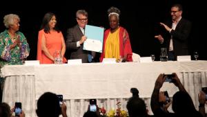 Foto da mesa de honra, com o reitor mostrando o título concedido a Conceição Evaristo